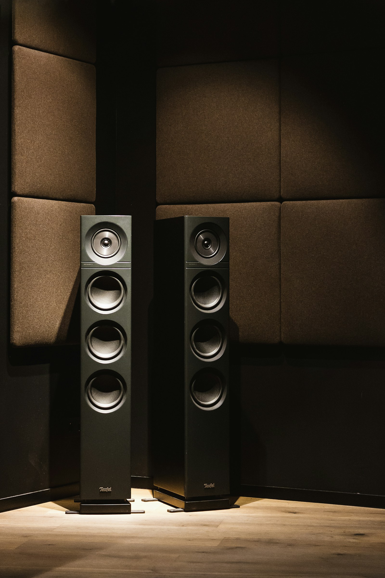 A pair of floor-standing loudspeakers in a fully treated listening room, oak floor underfoot.