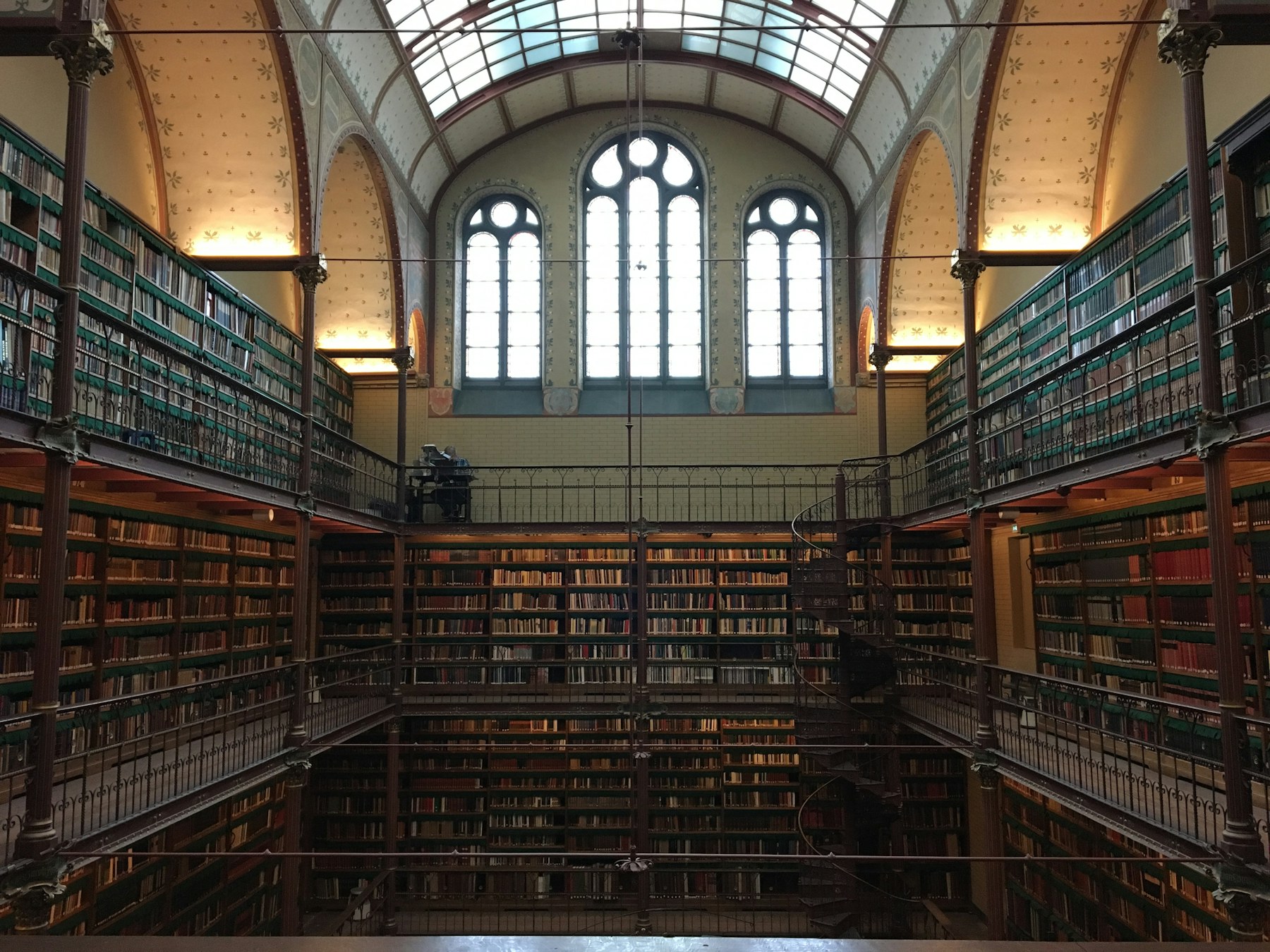 A multi-story reference library — green-leather books, wood balconies, arched windows above.