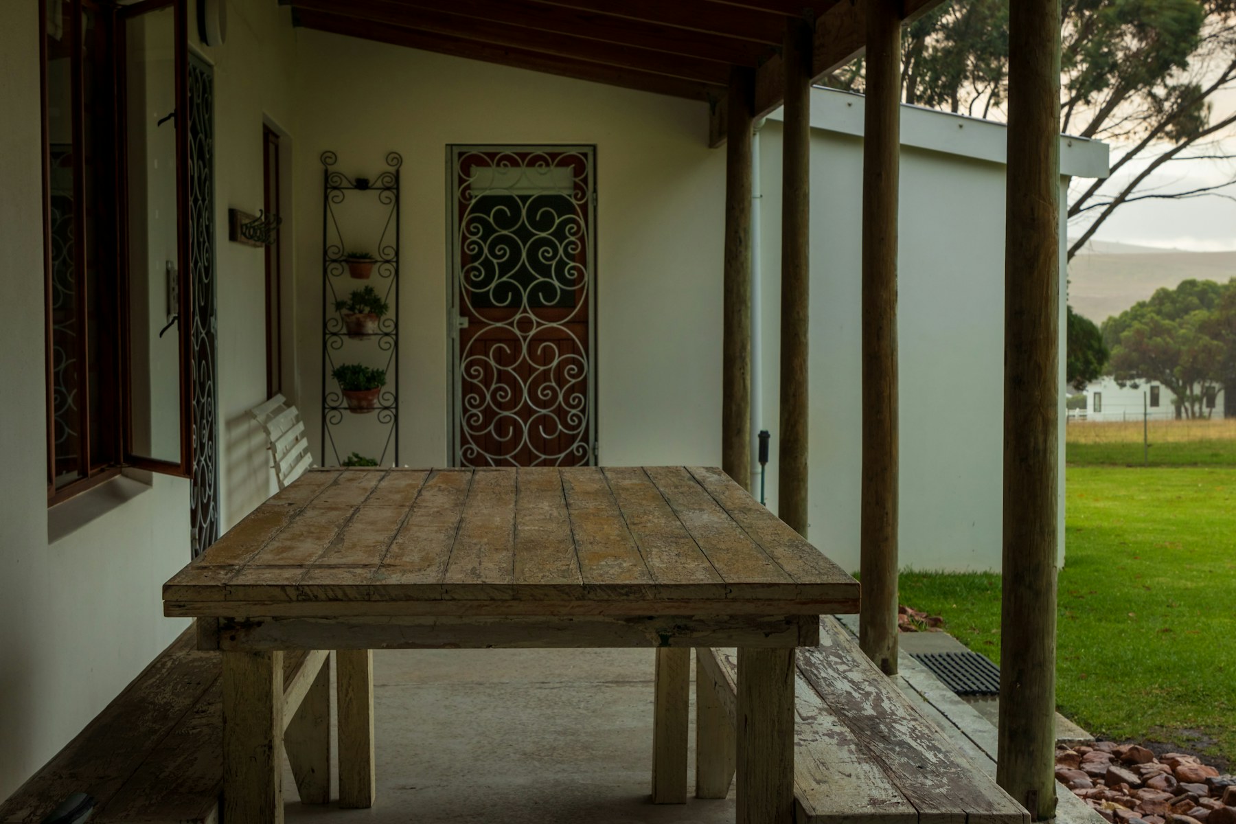 A long verandah with a weathered cypress table, set out under cool morning shade.