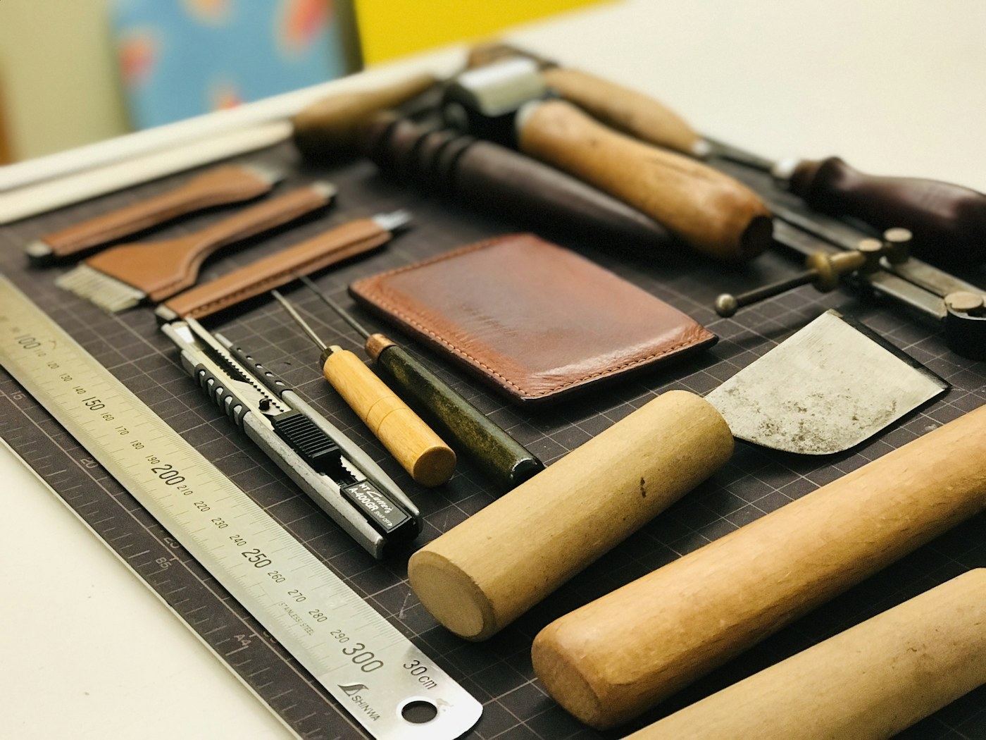 A workbench laid with leather-craft tools, wooden mallets, brass scribes, and a steel ruler — the small instruments behind specification work.